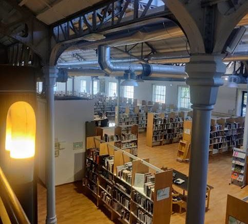 Ein großer Raum in einem ehemaligen Fabrikgebäude mit vielen hohen und langen Bücherregalen.