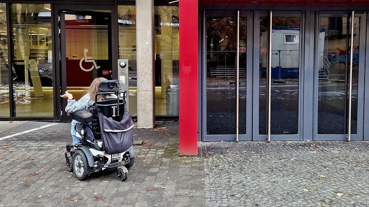 Laura Isbanner in ihrem Rollstuhl vor der barrierefreien Eingangstür am TIB-Standort Technik/Naturwissenschaften