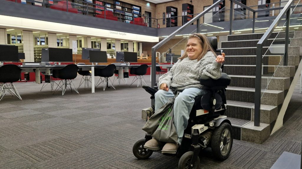 Laura Isbanner in ihrem Rollstuhl am Fuß der Treppe in der TIB