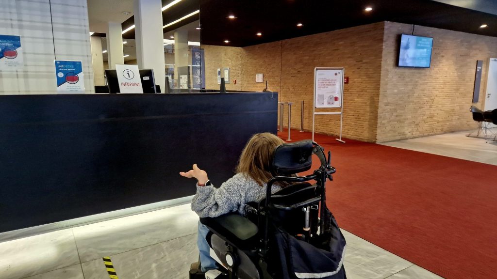 Laura Isbanner in ihrem Rollstuhl vor dem hohen Tresen im Eingangsbereich der TIB. 