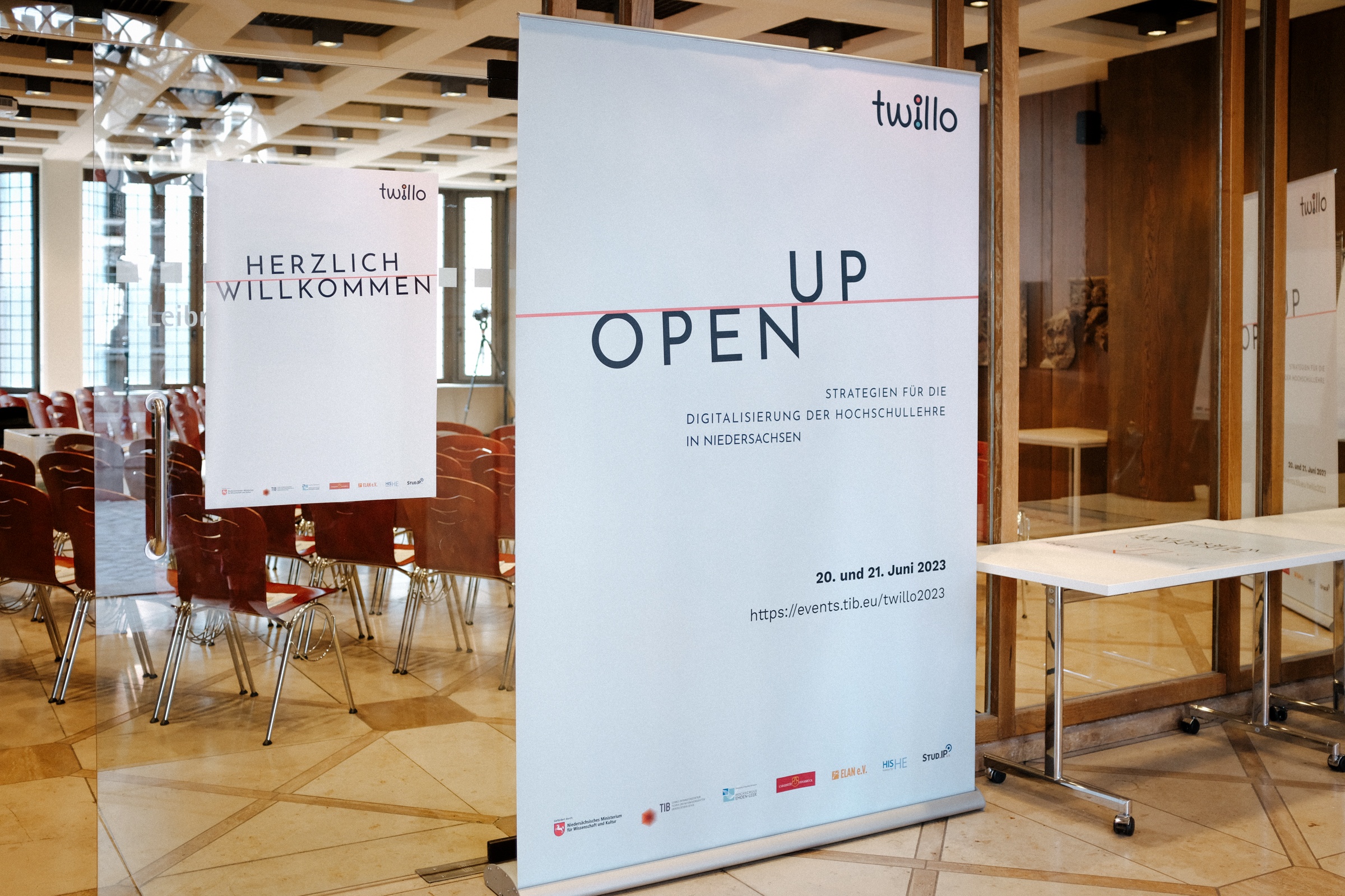 Foto von einem leeren Konferenzraum, vor dem ein Aufsteller mit der Aufschrift „Open Up“ steht.